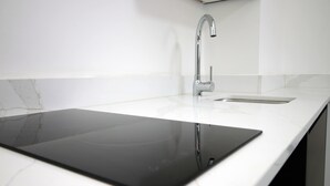 Une cuisine moderne dotée d’un élégant plan de travail noir, d’un robinet en acier inoxydable et d’un pare-feu en marbre blanc.