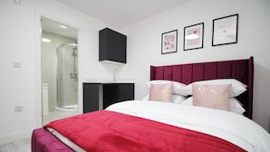 Une chambre avec un grand lit, une douche à l’italienne, une armoire noire et trois tableaux encadrés accrochés au mur.