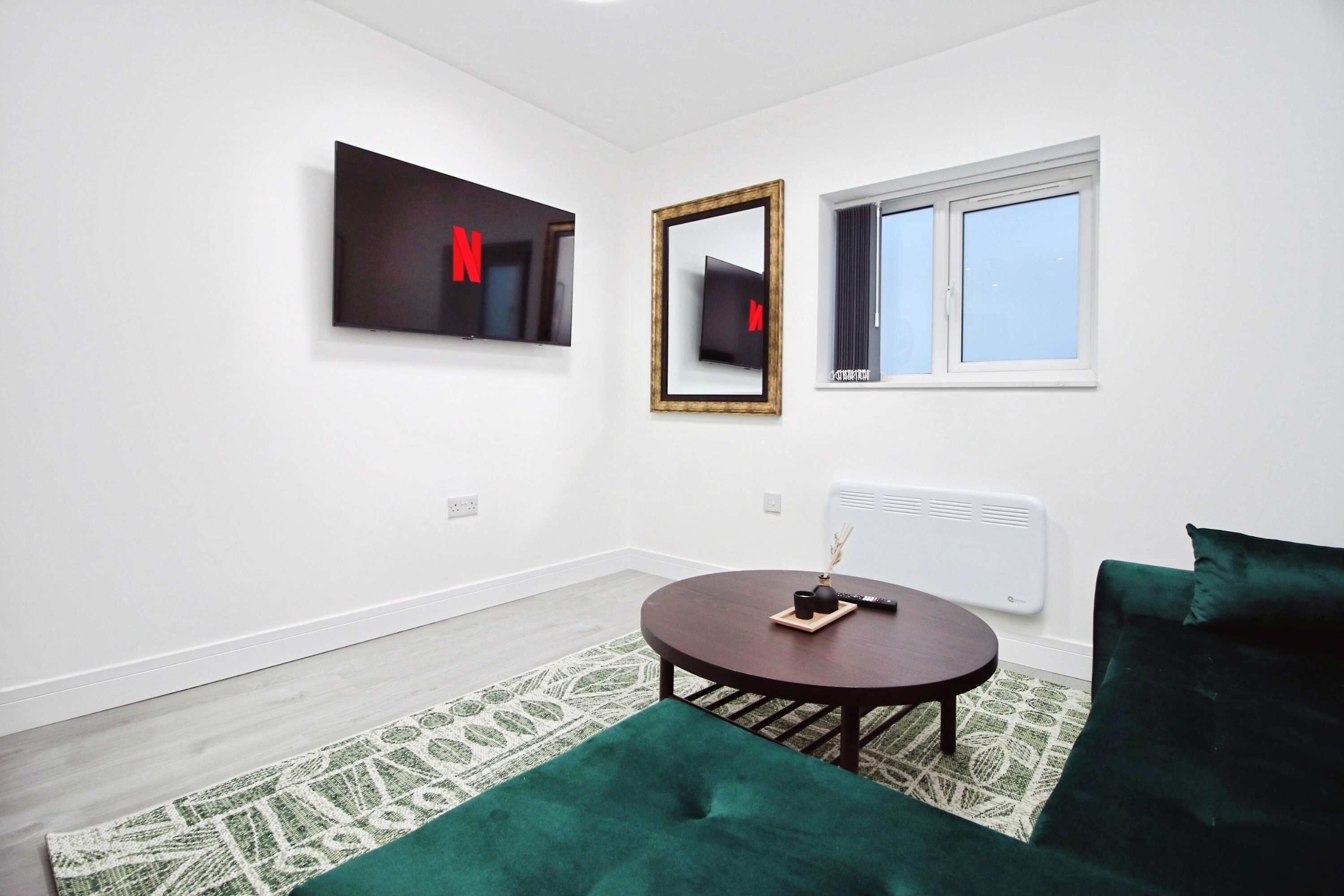 A modern living room with a round table, a green sofa, a mirror, and a TV mounted on the wall.