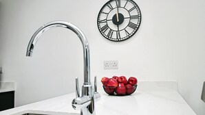 Une cuisine dotée d’un robinet moderne, d’une horloge murale et d’un saladier rempli de pommes rouges posé sur le comptoir.