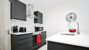 Une cuisine moderne avec des meubles noirs, un plan de travail blanc, un évier en acier inoxydable, une horloge au mur et une serviette rouge accrochée à la porte du four.