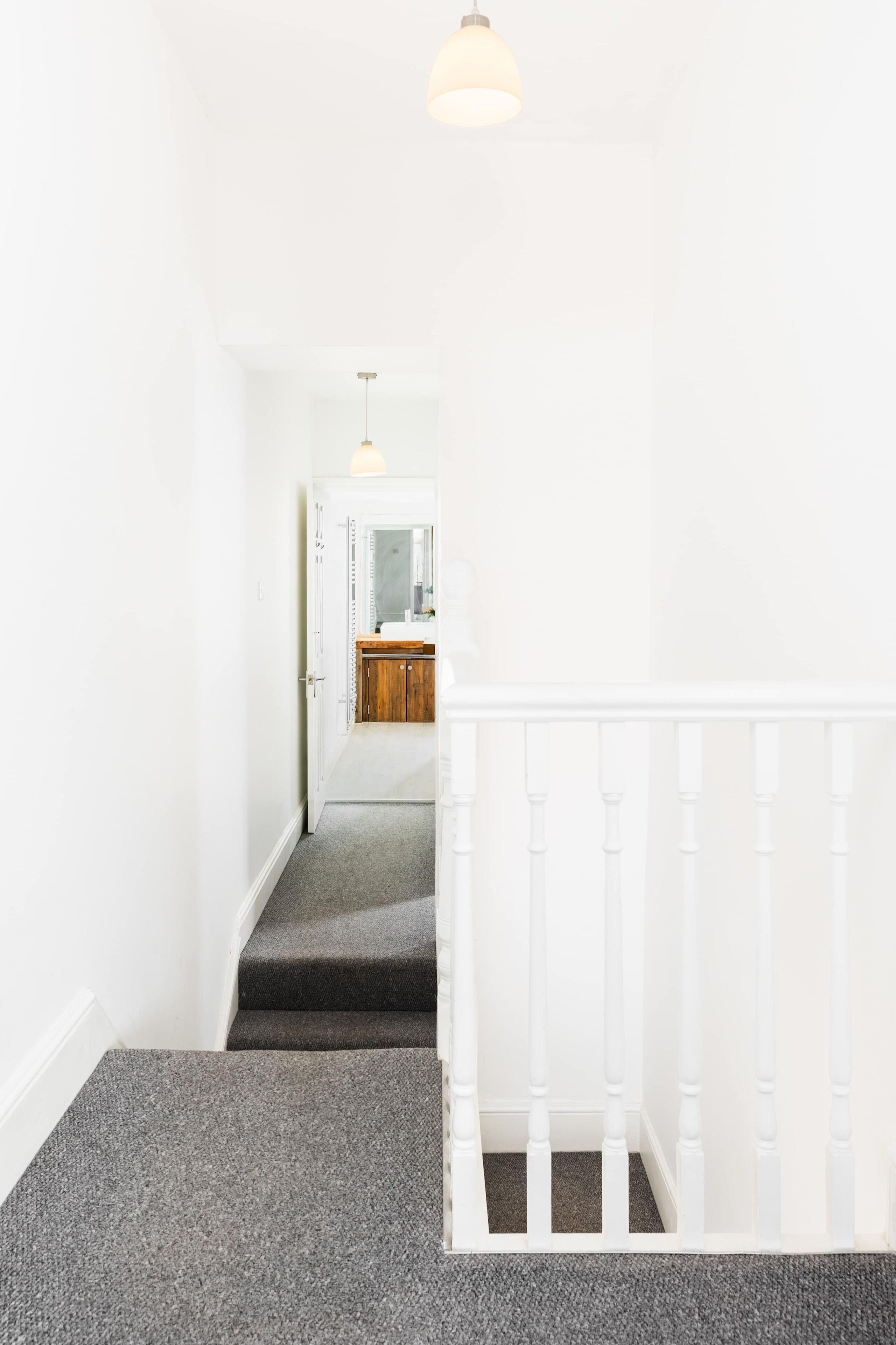 Eine Treppe mit weißer Brüstung, Teppichstufen und einer Leuchte darüber.