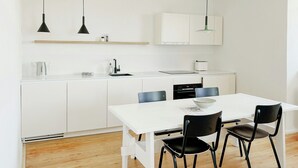 Eine moderne Küche mit weißen Schränken, einer weißen Arbeitsplatte, zwei Pendelleuchten, einem Wasserkocher, einem Toaster und einem Esstisch mit vier Stühlen.