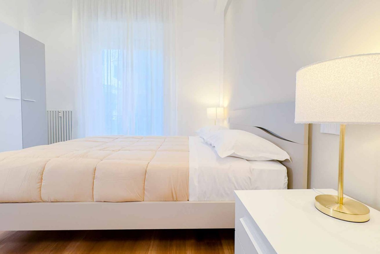 Et moderne hotelværelse med seng, sengebord, lampe og vindue med gardiner.