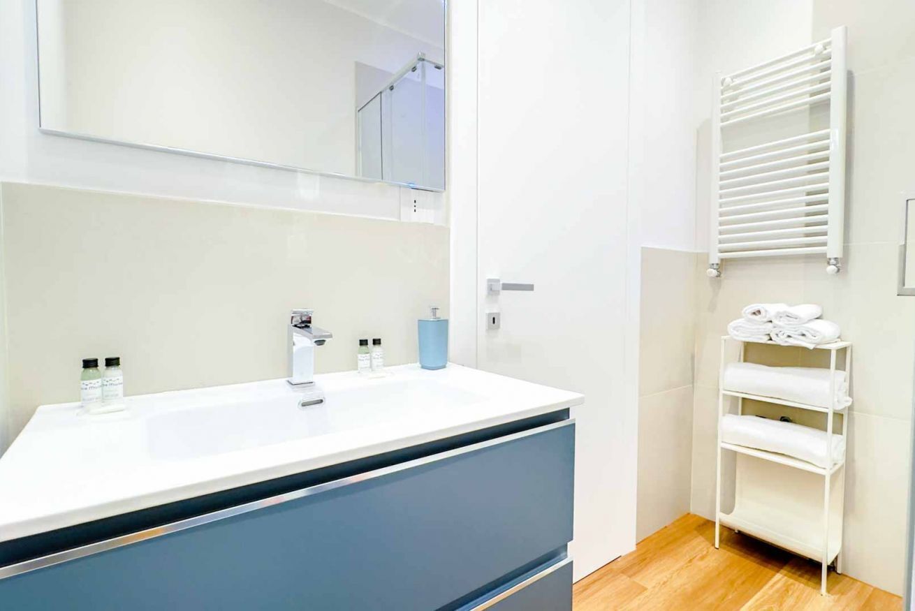 Ein modernes Badezimmer mit einem weißen Waschbecken, blauen Schränken, einem Spiegel und einem Handtuchhalter.