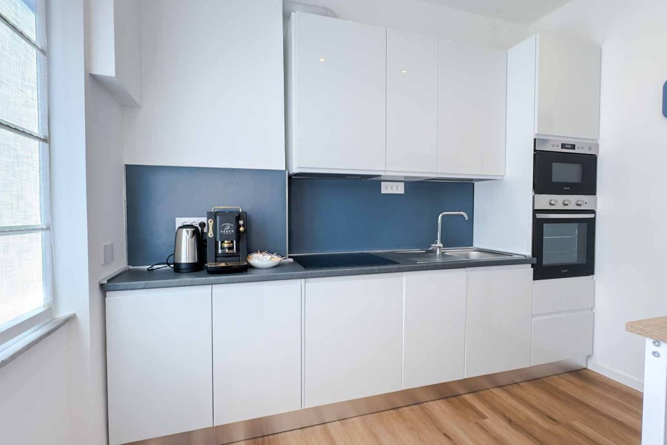 Una cucina moderna con mobili bianchi, un piano di lavoro nero, una macchina da caffè e forni a incasso.