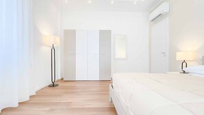 Un dormitorio minimalista con cama, lámparas de noche, un armario y un equipo de aire acondicionado.