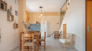 A dining area with a wooden table and chairs, a refrigerator, and a wicker chair. - Panoramablick auf das Libysche Meer im SeaCrete House! (Keratokampos)