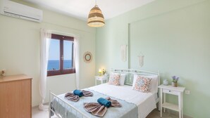 A bedroom with a bed, bedside tables, a dresser, a window with curtains, and a hanging light fixture. - Panoramablick auf das Libysche Meer im SeaCrete House! (Keratokampos)