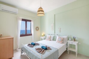 A bedroom with a bed, bedside tables, a dresser, a window with curtains, and a hanging light fixture. - Panoramablick auf das Libysche Meer im SeaCrete House! (Keratokampos)