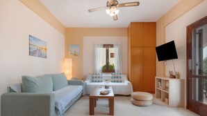 A living room with a sofa, a coffee table, a television, and a window with curtains. - Panoramablick auf das Libysche Meer im SeaCrete House! (Keratokampos)