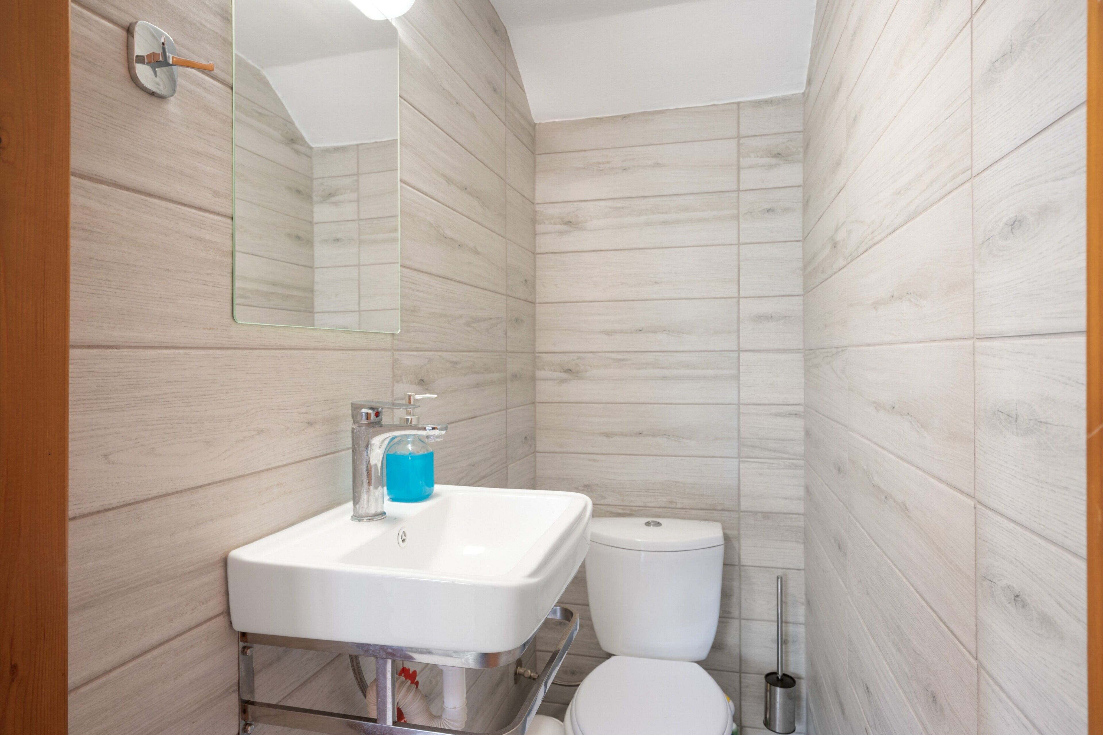 Un baño con lavamanos, espejo y váter frente a una pared de madera.