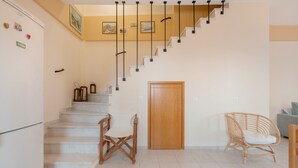 A staircase with a wooden door at the bottom, a wicker chair, and a refrigerator. - Panoramablick auf das Libysche Meer im SeaCrete House! (Keratokampos)