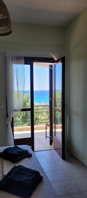 A room with a bed, a window with a view of the sea, and a balcony.