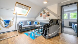 Quarto estilo loft com sofá, poltrona de massagem, cadeira suspensa, mesinha e vista para o exterior.