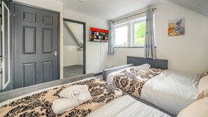 Quarto de hotel com duas camas, janela com cortinas, radiador, TV fixada na parede e escada que leva a outro cômodo.