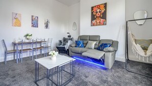 Un saló modern amb un sofà gris, una taula de dinar amb cadires, una taula auxiliar i una cadira espanyola.