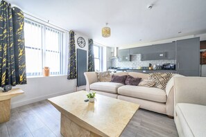 Un salon moderne avec un canapé beige, une table basse et une cuisine en arrière-plan.