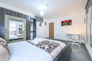 Une chambre moderne avec un grand lit, une armoire, un bureau et un panneau Netflix fixé au mur.