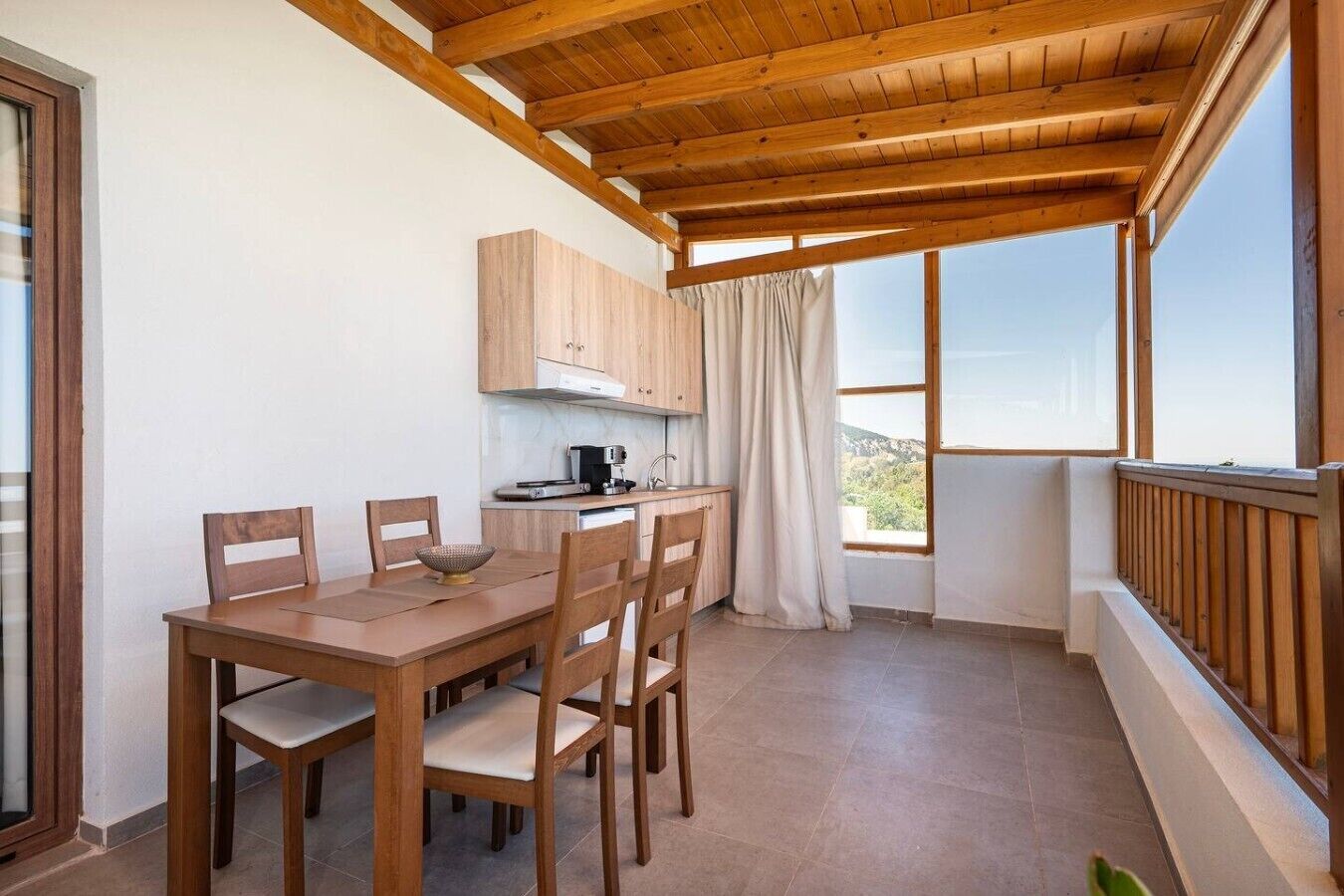 A dining area with a wooden table and chairs, a kitchen with cabinets, and a view through a window.