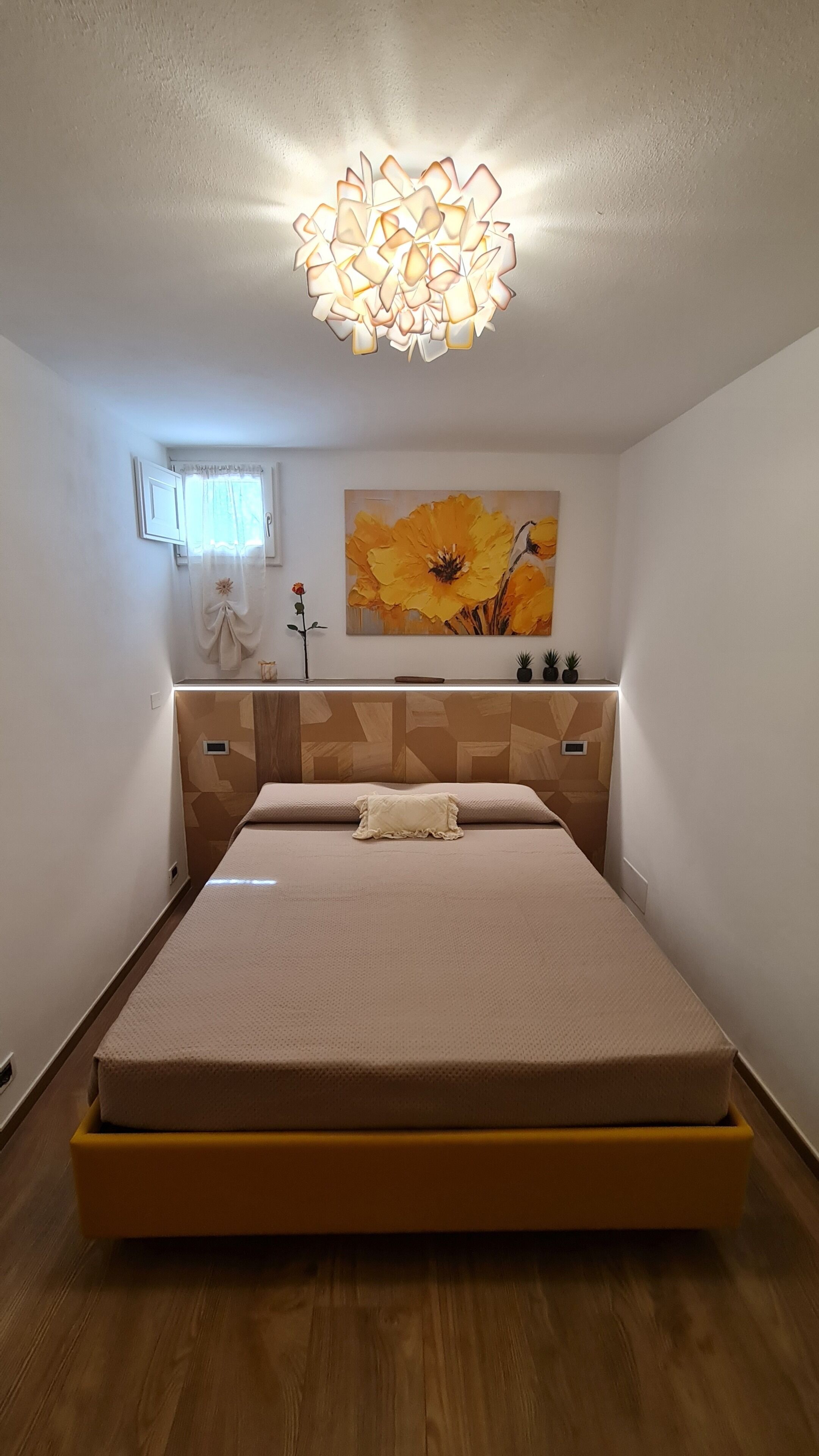 Een moderne slaapkamer met een bed, een aan de muur bevestigd kunstwerk, een plafondlamp en een raam met gordijnen.