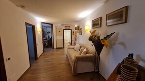 Un pasillo con piso de madera, un sofá, un florero con flores y cuadros en la pared.