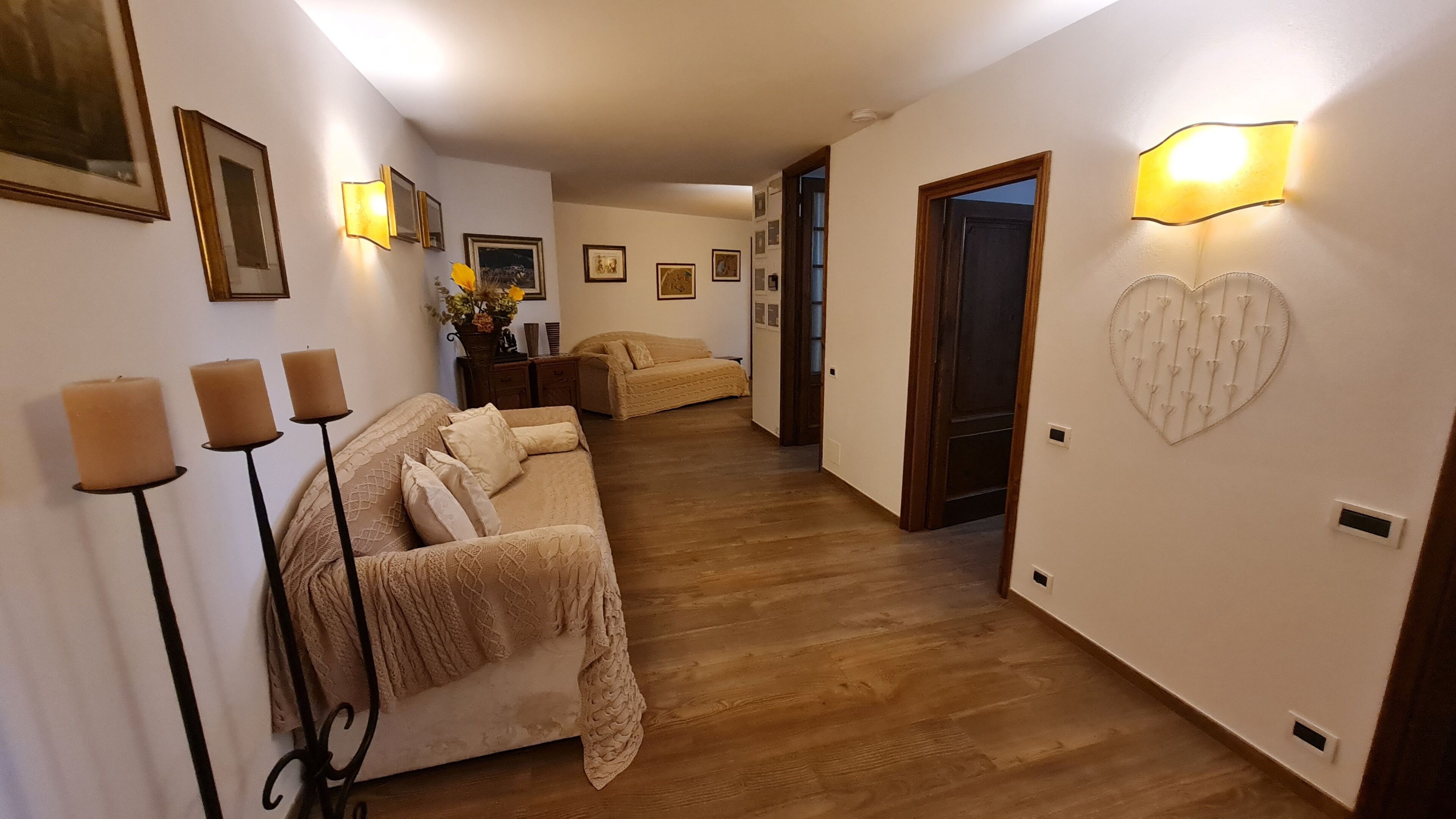 A hallway with a sofa, wall-mounted lights, framed pictures, and a heart-shaped light fixture.