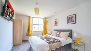 Une chambre à coucher avec un lit, une table de chevet avec une lampe, une armoire, une fenêtre avec des rideaux et des œuvres d’art accrochées au mur.