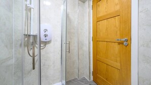 Une douche fermée par des parois en verre, dotée d’un pommeau de douche à main et d’un distributeur de savon.