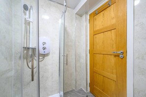 Une douche fermée par des parois en verre, dotée d’un pommeau de douche à main et d’un distributeur de savon.