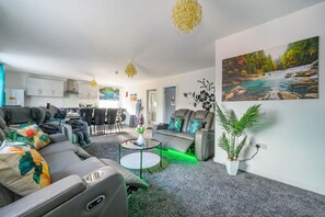 A modern living room with a sofa, a coffee table, and a dining area with chairs. - F2TR- Captivating & Peaceful Stay (West Yorkshire)