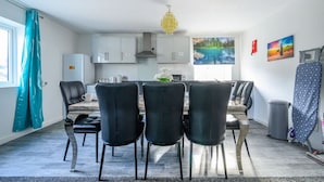 Une cuisine moderne avec des meubles blancs, un coin repas avec des chaises noires et une grande fenêtre ornée d’un tableau.