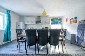 A modern kitchen with white cabinets, a dining area with black chairs, and a large window with a painting. - F2TR- Captivating & Peaceful Stay (West Yorkshire)