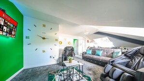 A modern living room with a green accent wall, a wall clock, a massage chair, a sofa, and a coffee table. - Stylish Home for 6 in West Yorkshire (West Yorkshire)