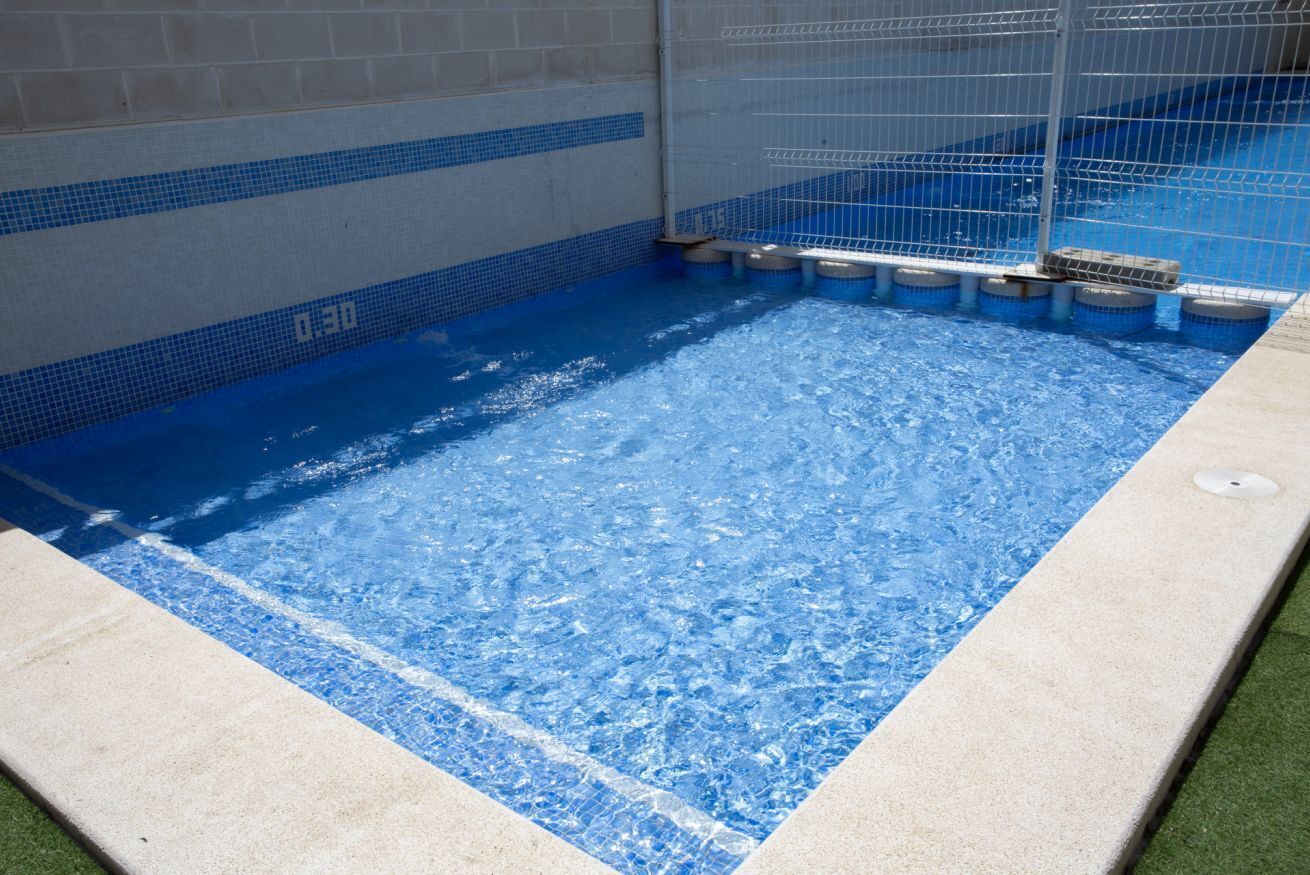 Ein Schwimmbecken mit Fliesenrand und einem Metallschutzzaun.