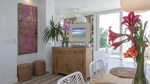 Uma sala de estar moderna com um aparador de madeira, cadeiras de vime, uma mesa de jantar e uma janela grande com vista.