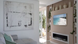 Uma sala de estar com um grande quadro abstrato, um sofá, uma lareira e uma cena de praia na parede.