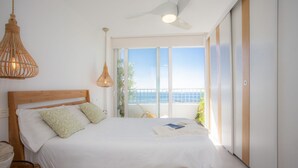 Quarto com cama de madeira, ventilador de teto e vista para o oceano.