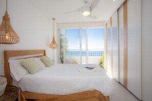 Ein Schlafzimmer mit einem hölzernen Bett, einem Deckenventilator und Blick aufs Meer.
