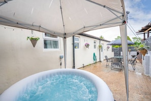 Un jacuzzi exterior bajo una cubierta, rodeado de muebles de patio y cestas de flores colgantes.