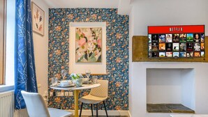 Ein Essbereich mit rundem Tisch, Stühlen und einer an der Wand befestigten Netflix-Anlage.