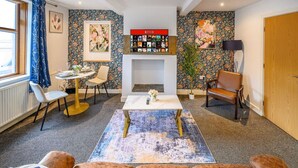 Ein Wohnzimmer mit Kamin, Couch, Esstisch mit Stühlen, Couchtisch und Bücherregal.