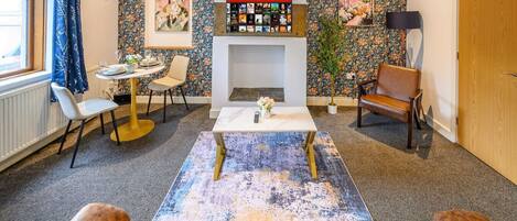 Una sala de estar con chimenea, una mesa de centro, un sofá, una mesa de comedor con sillas y una estantería.