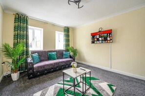 Een woonkamer met een bank, een salontafel, een aan de muur bevestigd Netflix-scherm en een vloerkleed met dessin.