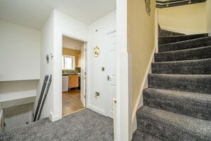 A staircase leading to a second floor, a kitchen area with wooden cabinets, and a door with a circular decoration. - H17A Cosy & Welcoming home (West Yorkshire)