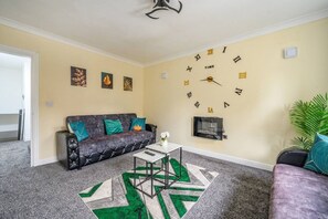 Een woonkamer met een bank, een salontafel, een wandklok en een televisie.