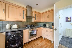 A compact kitchen with wooden cabinets, a built-in oven, a washing machine, and a small countertop with a kettle and toaster. - H17A Cosy & Welcoming home (West Yorkshire)