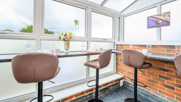 A conservatory with a brick wall, a glass table, and three brown chairs.