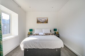A bedroom with a bed, two bedside tables, a window, a radiator, and a painting on the wall. - For Your most relaxed and cosy stay (West Yorkshire)