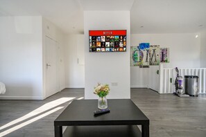 A hotel lobby with a black table, a vase with flowers, a wall-mounted Netflix display, and a vacuum cleaner. - For Your most relaxed and cosy stay (West Yorkshire)